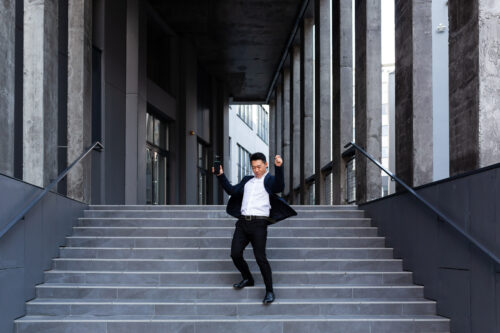 Happy and cheerful Asian businessman dancing near the office rejoices in victory and success